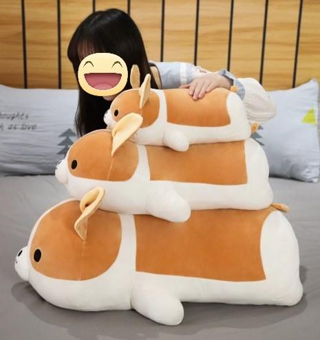 Image of a girl lying on the bed next to two Corgi stuffed animals soft plush toys in different sizes